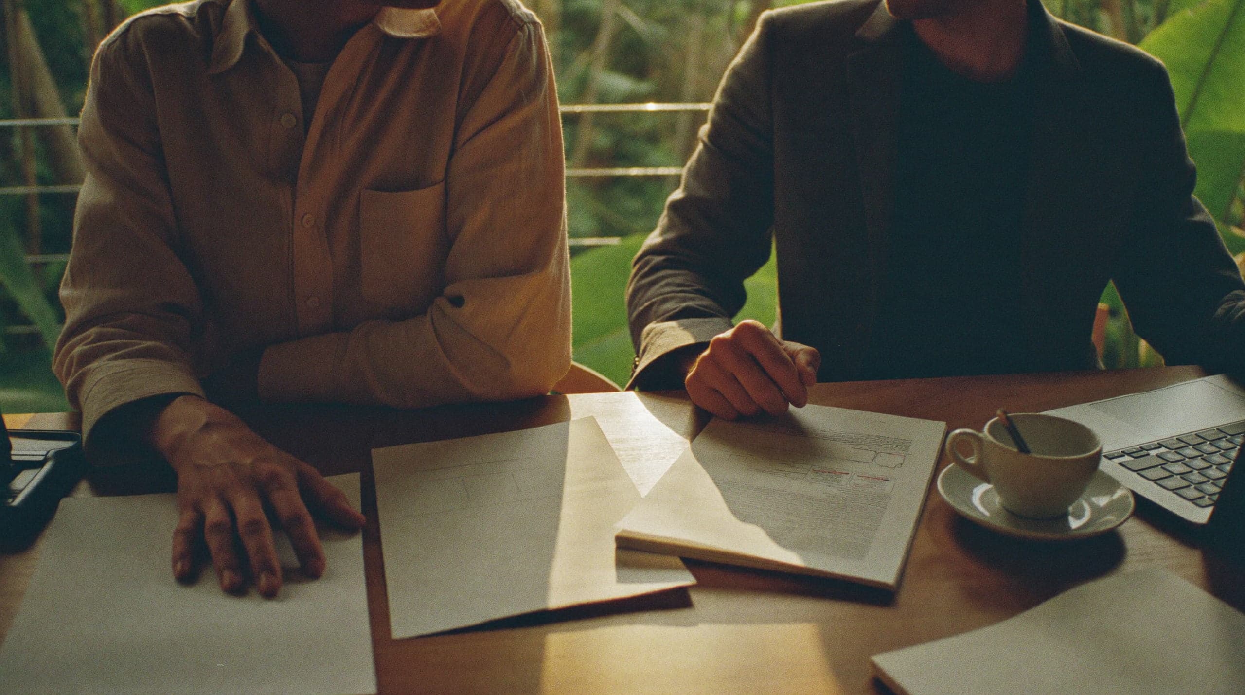 Two people at a table working through a marked-up printed document together, one pointing at a line, faces out of frame.