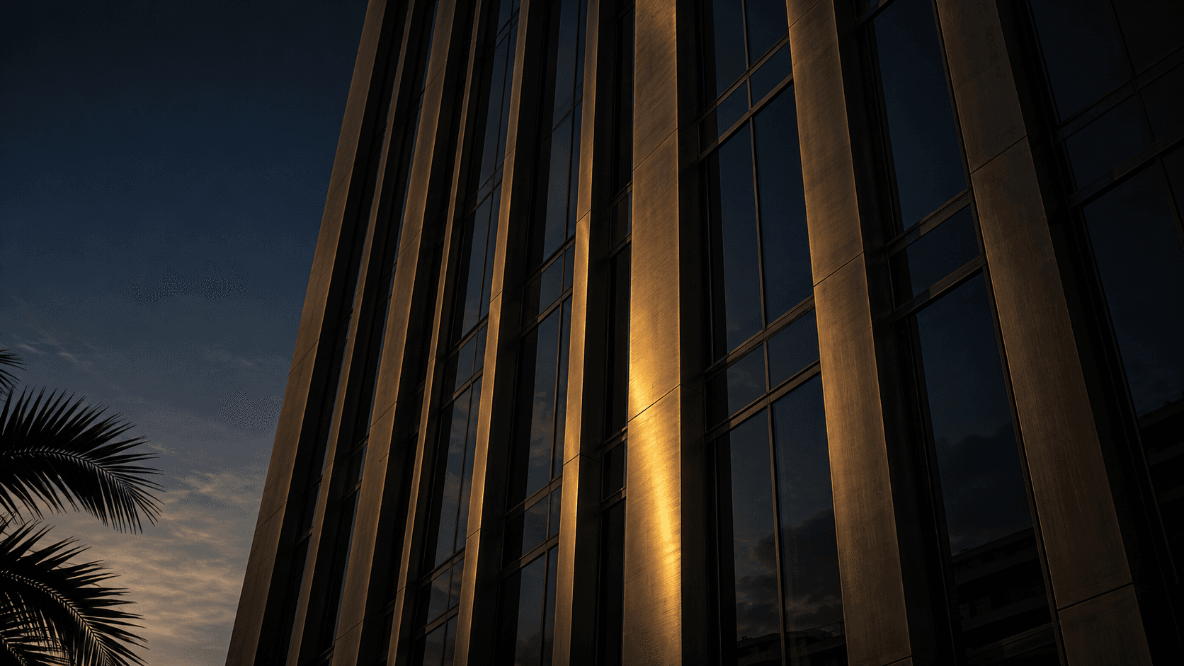 Downtown Miami office tower facade at twilight, brushed bronze louvers and a gold reflection against a dusk navy sky