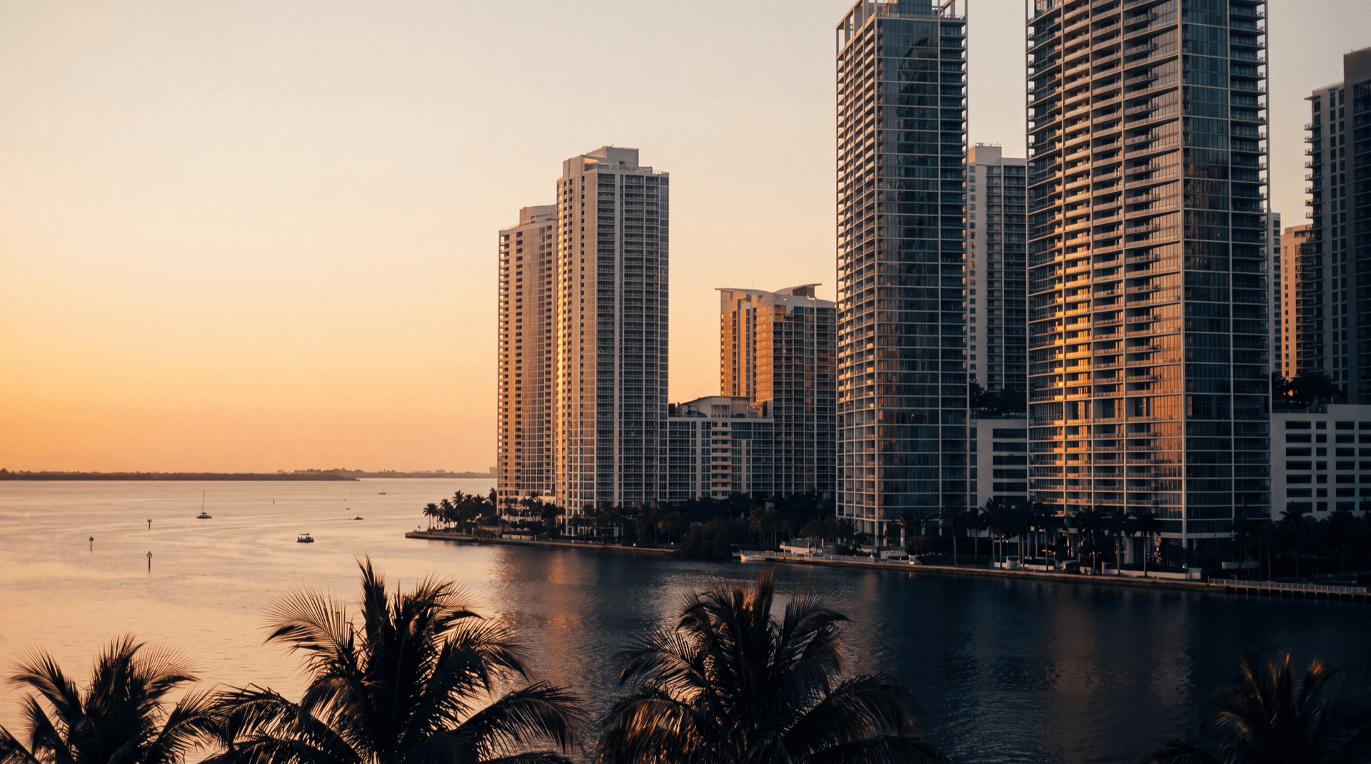 Brickell Miami skyline and waterfront at golden hour, palm trees silhouetted against warm sunset light over Biscayne Bay