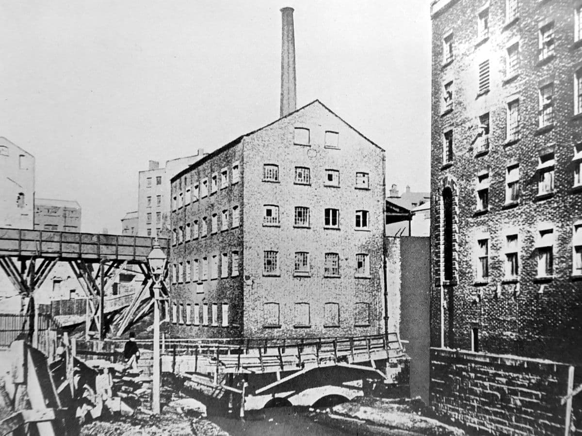 Grammar School Mills, Manchester, in a photograph published in 1908: a brick mill with a tall chimney, and the old bridge to Victoria Station.